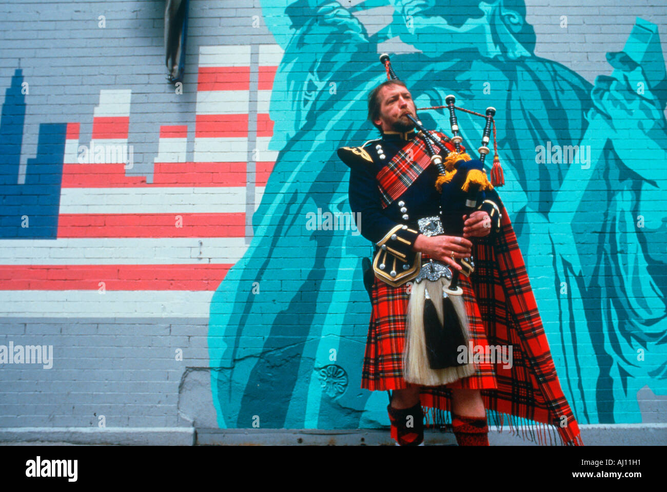 A man in kilt playing bagpipes in front of a patriotic mural St Patrick s Day Parade NY City Stock Photo