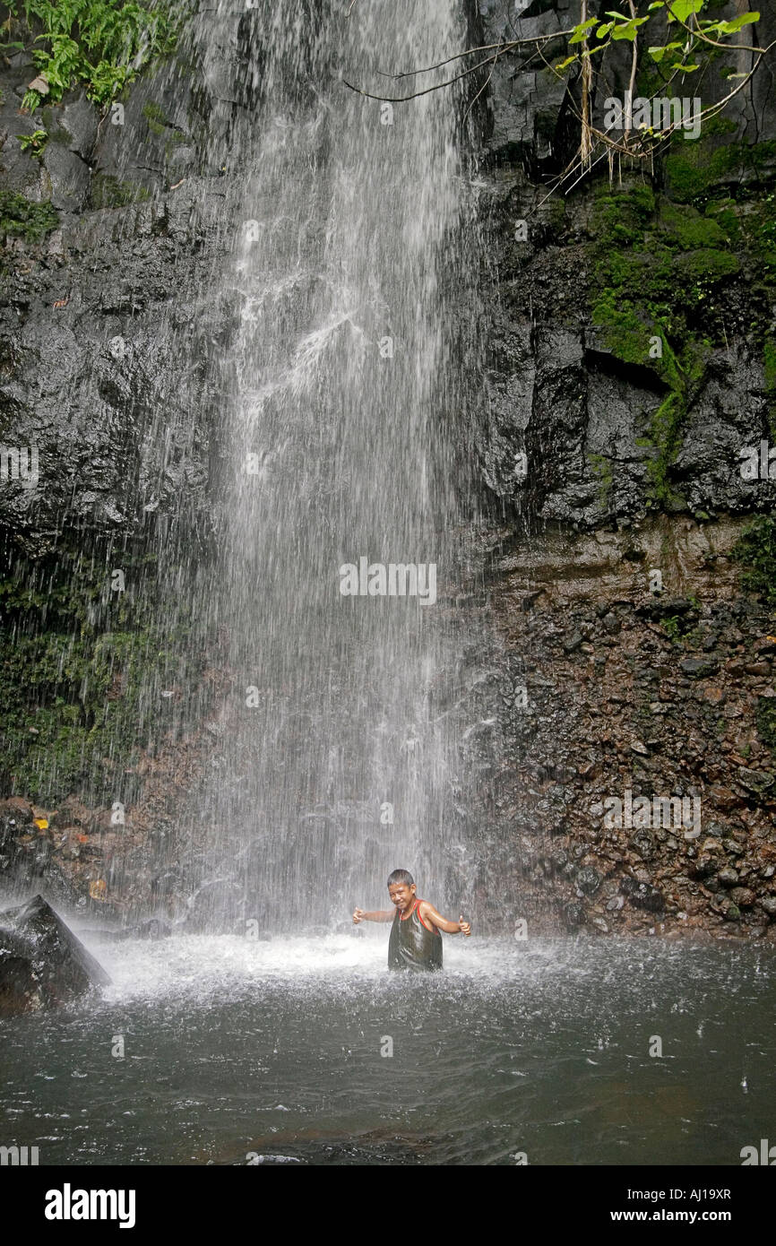 Young native boy plays in cascading spray of Sipyen Waterfall in Kosrae Federated States of Micronesia FSM Stock Photo