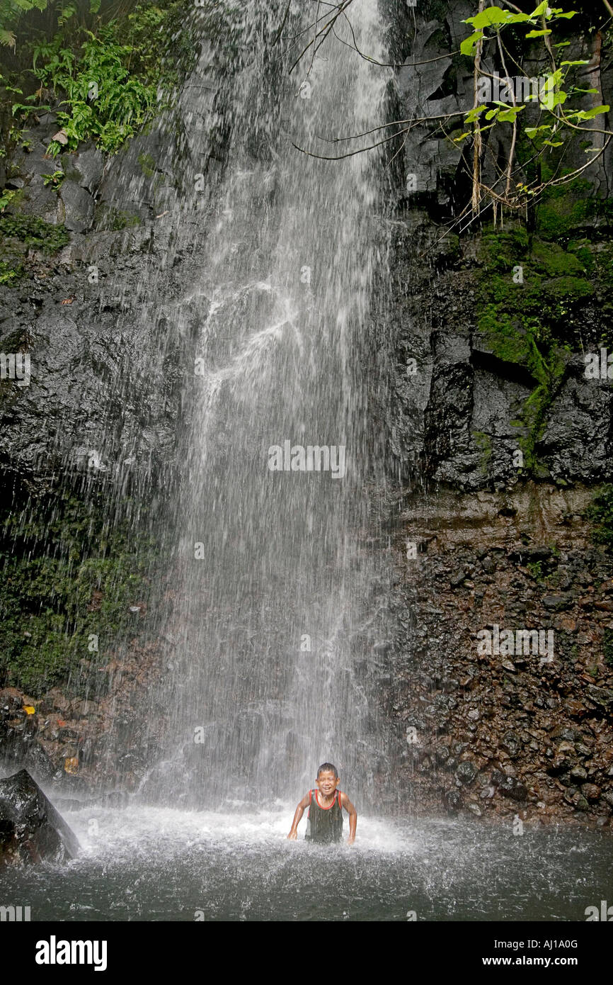 Young native boy plays in cascading spray of Sipyen Waterfall in Kosrae Federated States of Micronesia FSM Stock Photo