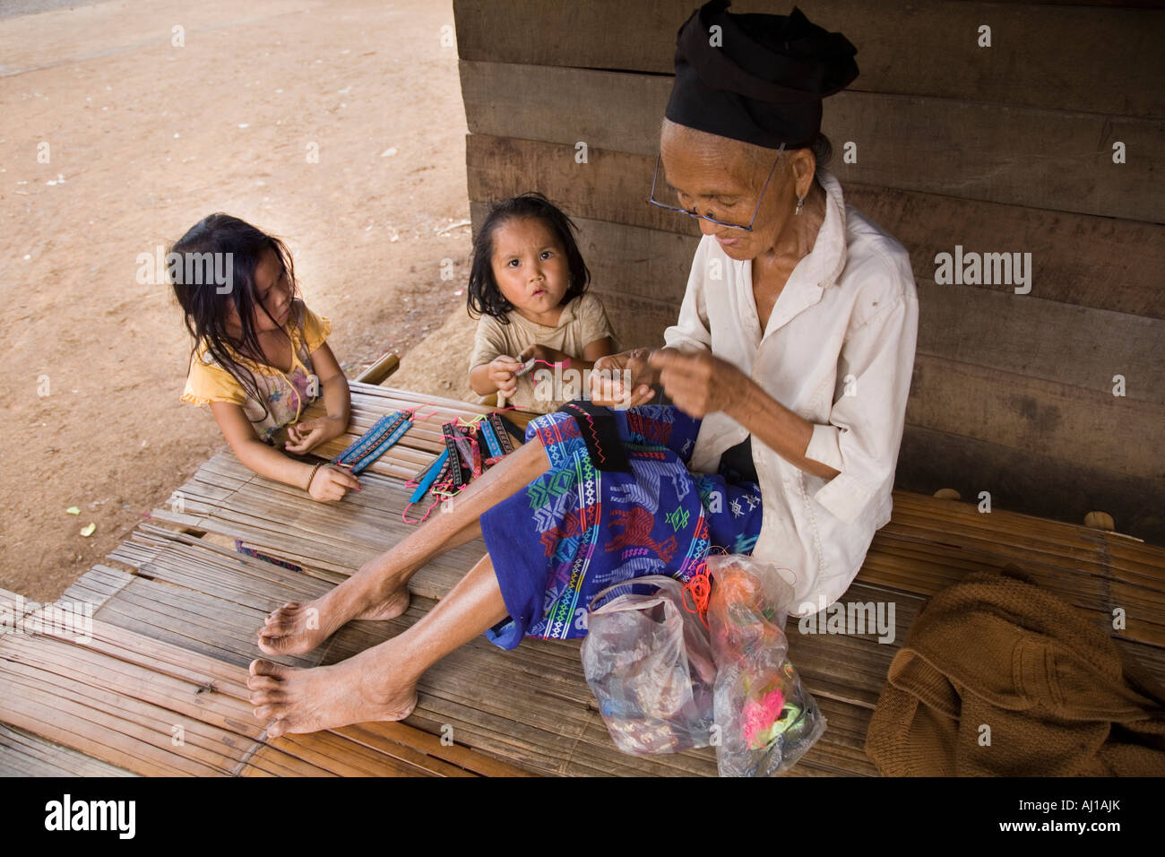 Children and elderly woman making wrist bands to sell tourists in Hmong tribal village near Luang Prabang Laos Stock Photo