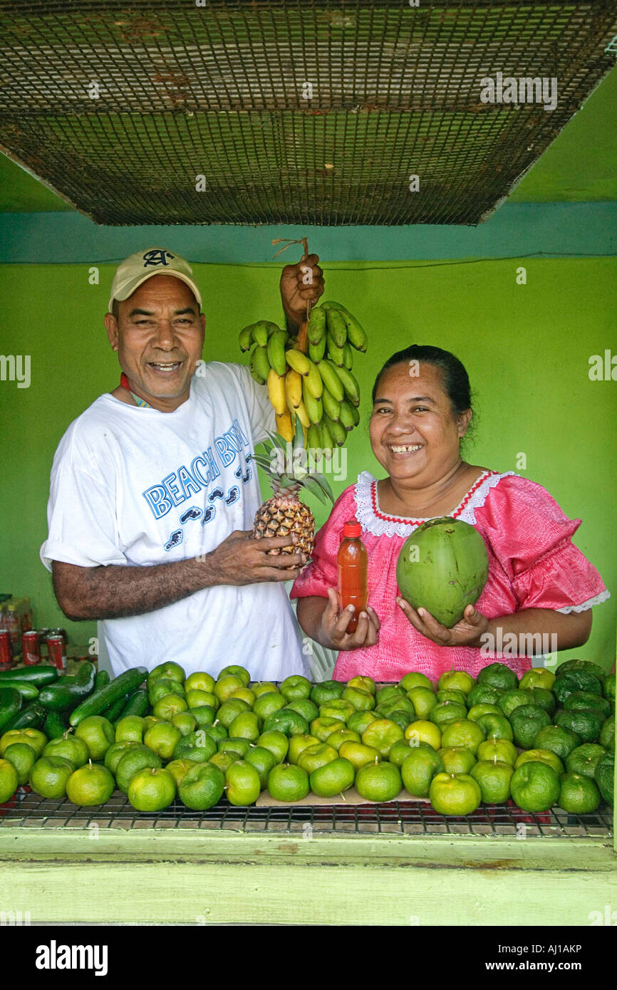 Kosrae man and wife show tangerines pineapple bananas coconut and coconut oil for sale at their fruit stand in Micronesia Stock Photo