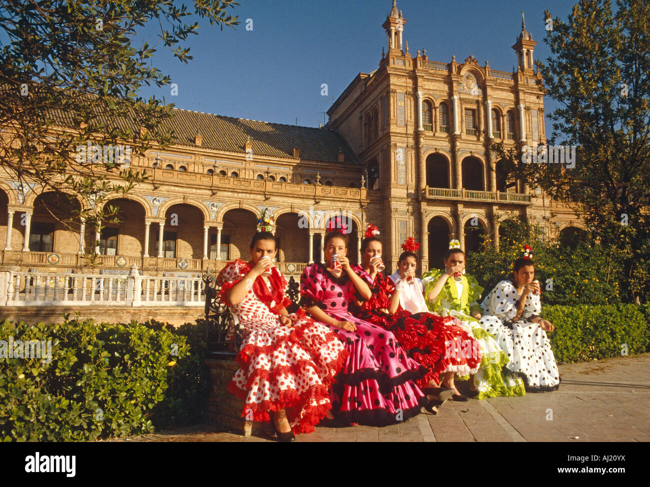 Spanish girls sitting on a bench dressed in flamenco costumes drinking