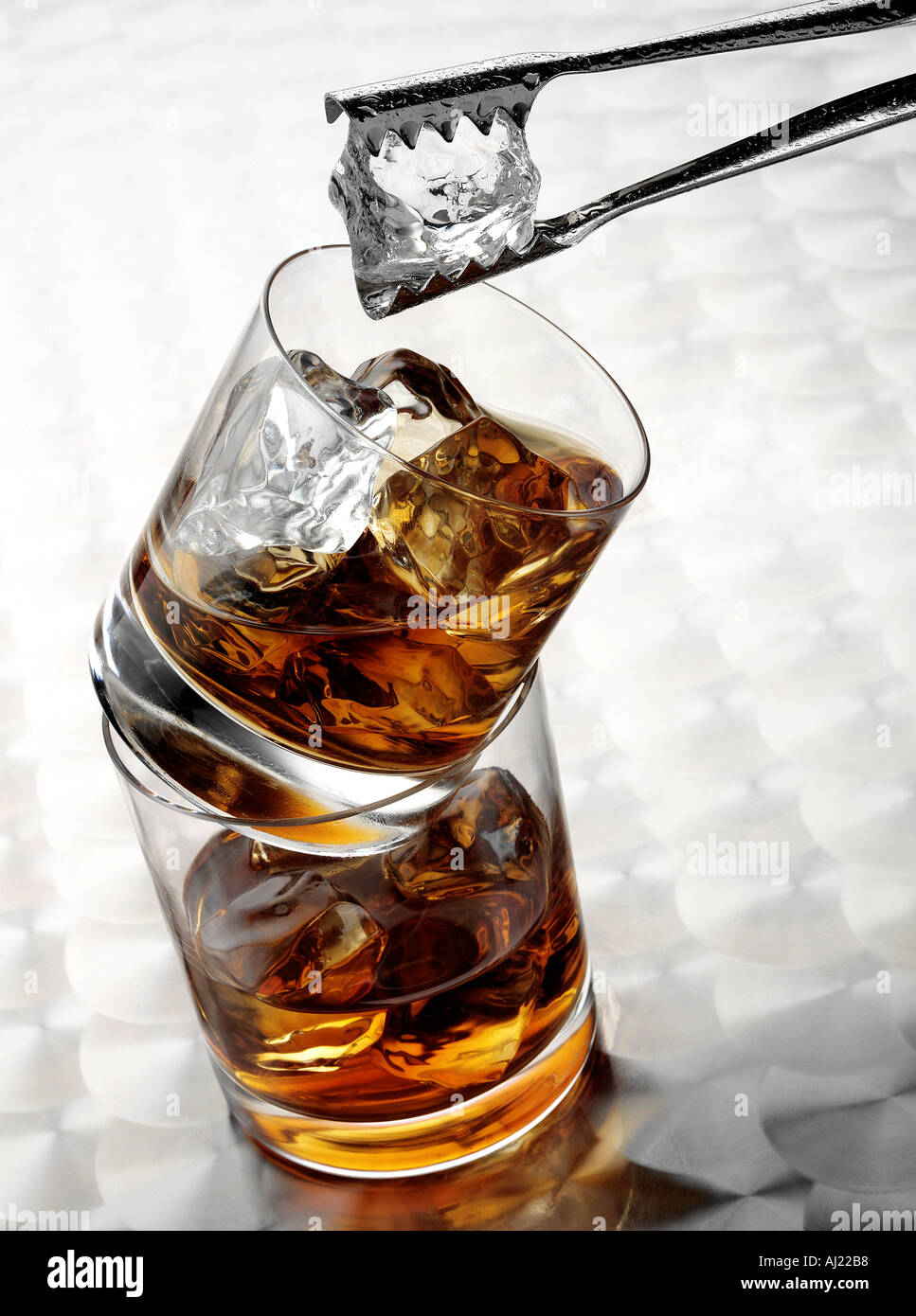 WHISKEY IN TWO GLASSES BALANCED ON TOP OF EACH OTHER. WITH ICE AND TONGS Stock Photo