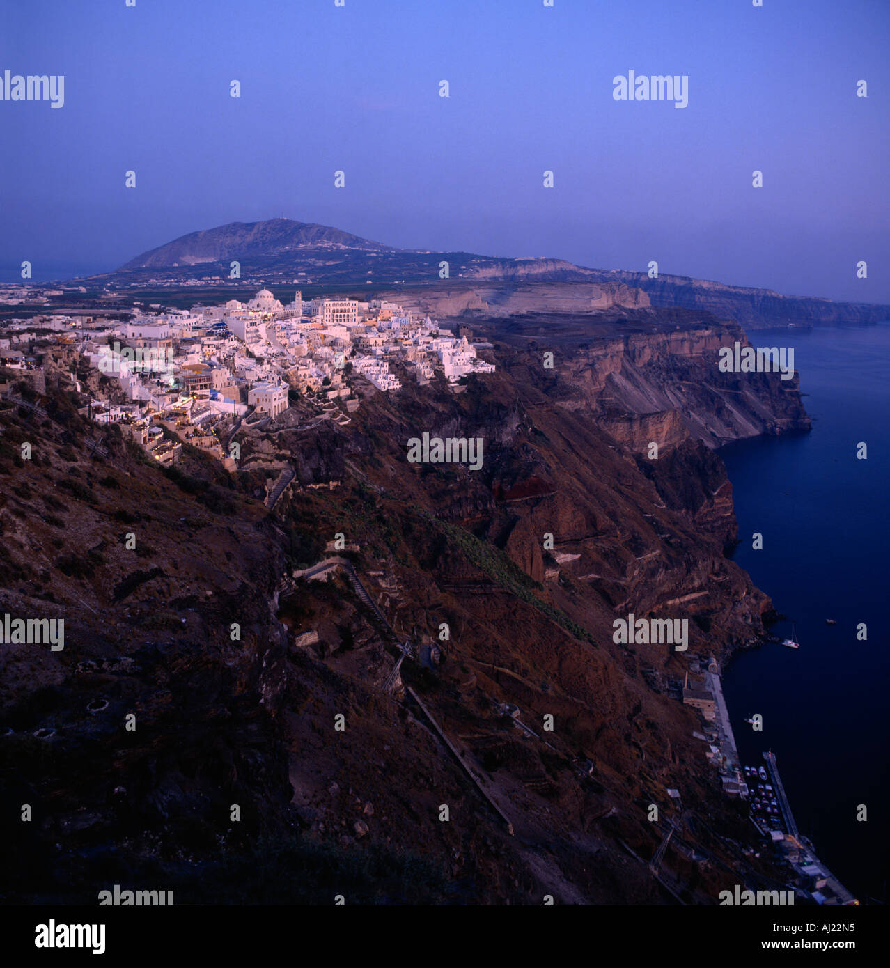 Looking across precipitous steep cliffs with white buildings on top & small harbour below Fira town Santorini The Greek Islands Stock Photo
