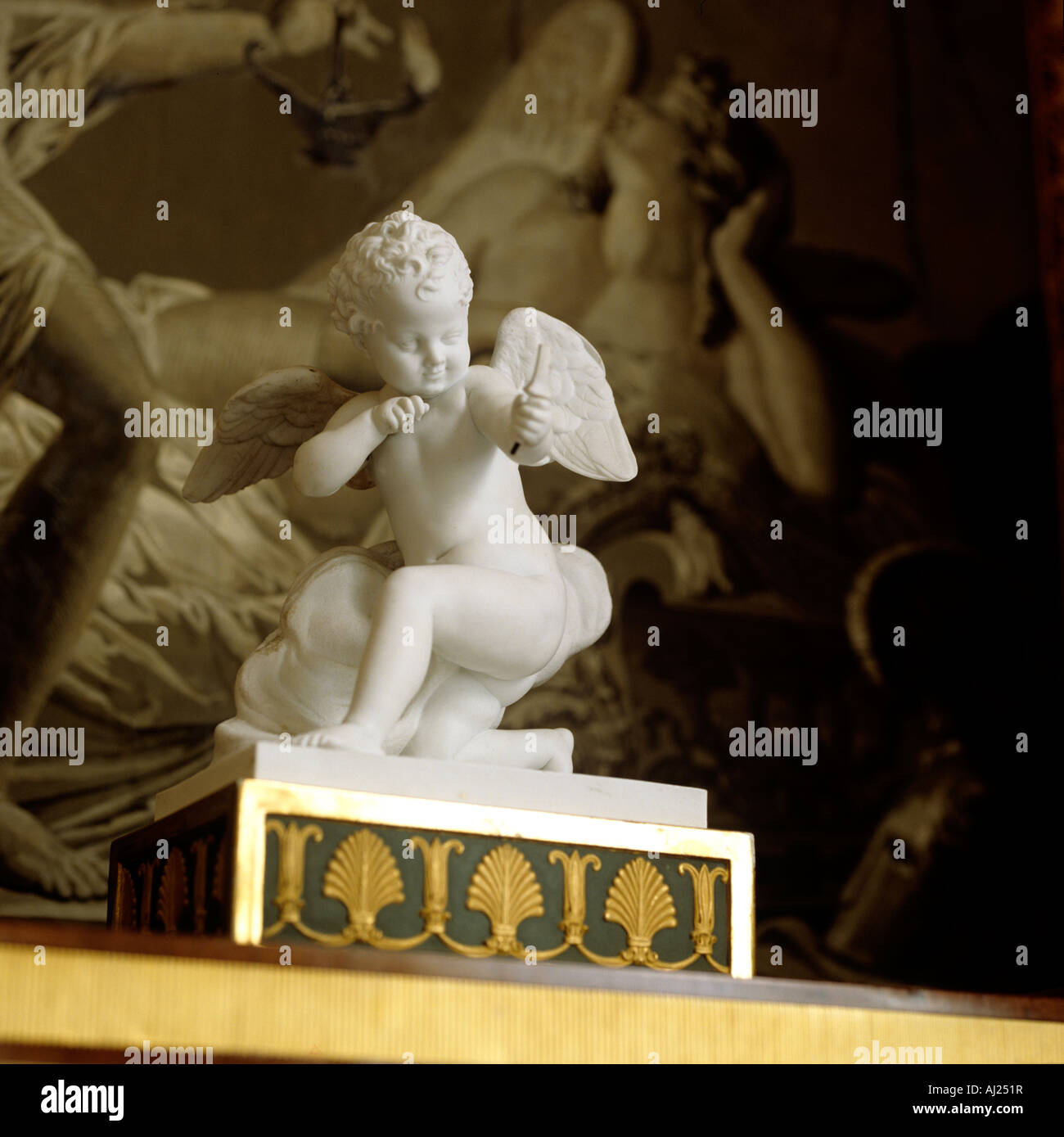 White marble cherub statue on ornate plinth with religious art in back ground Stock Photo