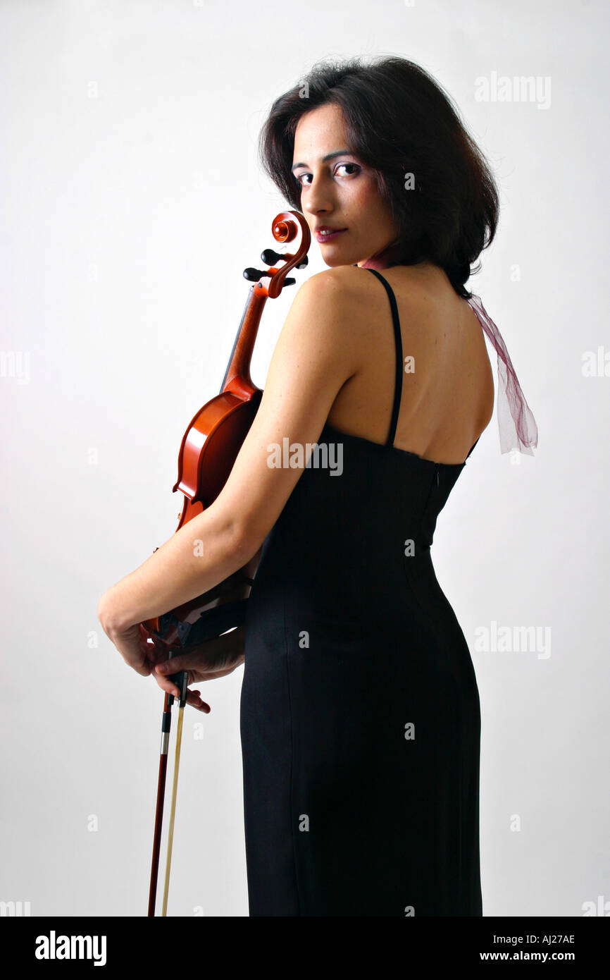 Medium shot of young woman in black evening gown holding a violin and looking coyly over her shoulder Stock Photo