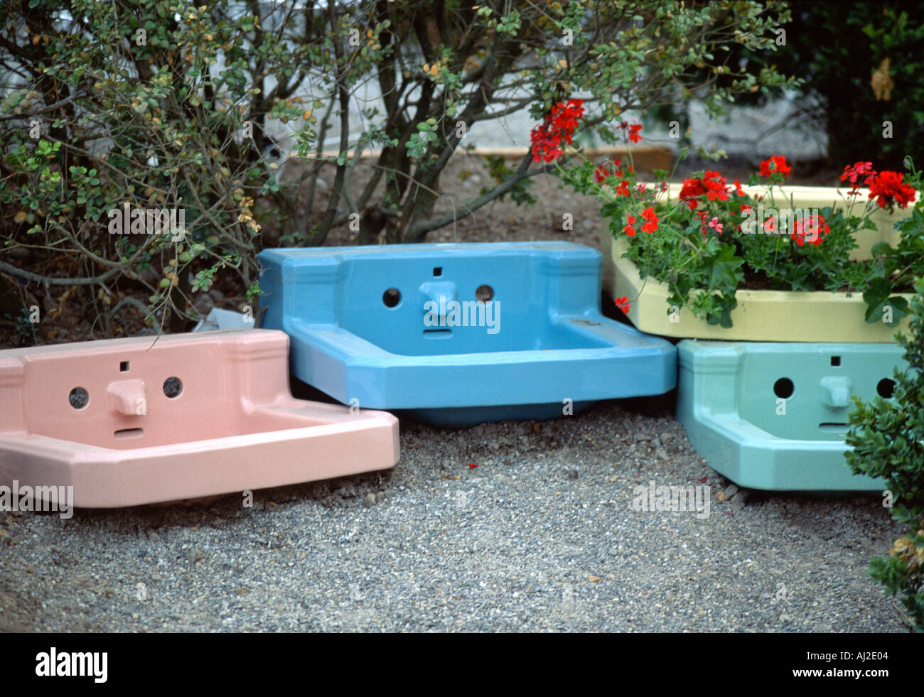 Four colorful vintage wash basins looking like faces of grumpy people recycled as decorative planters in a garden in Belgium Stock Photo