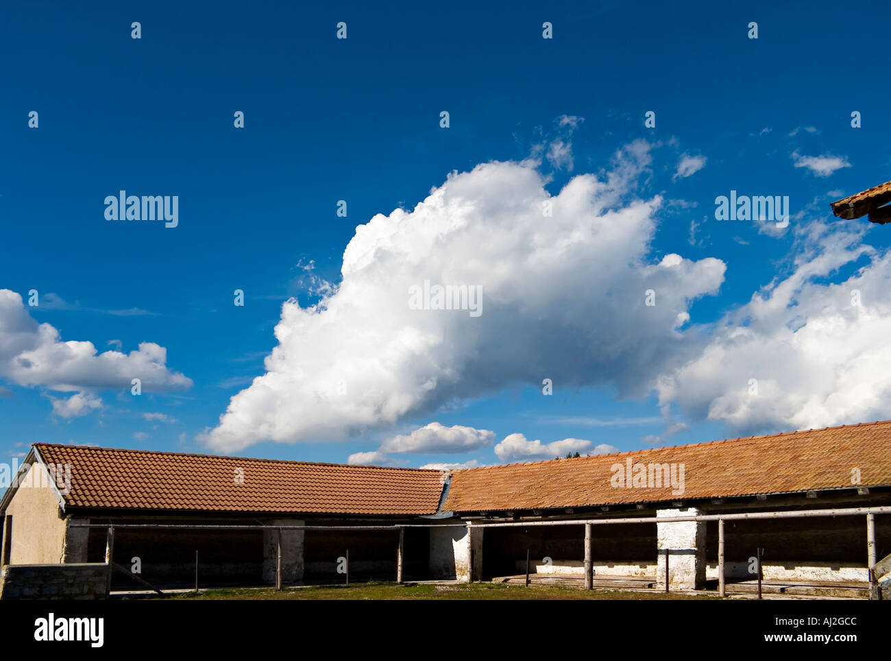 red mountain stable small farm with large roof and tile with blue sky and clouds Stock Photo