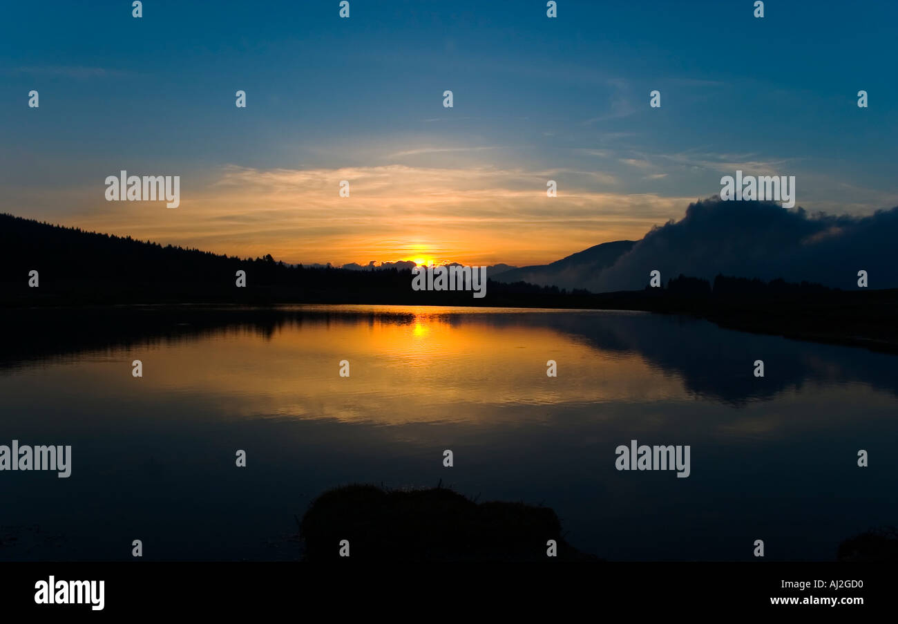 landscape sunset on small mountain lake with red sun that be mirrored and blue sky Stock Photo