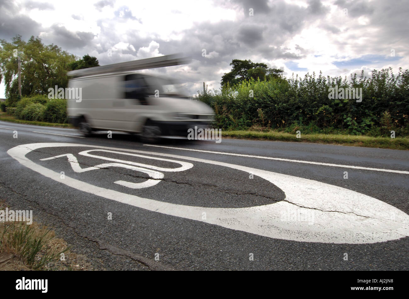 A blurred white van whizzes past a 30mph limit sign painted on a country road. Stock Photo