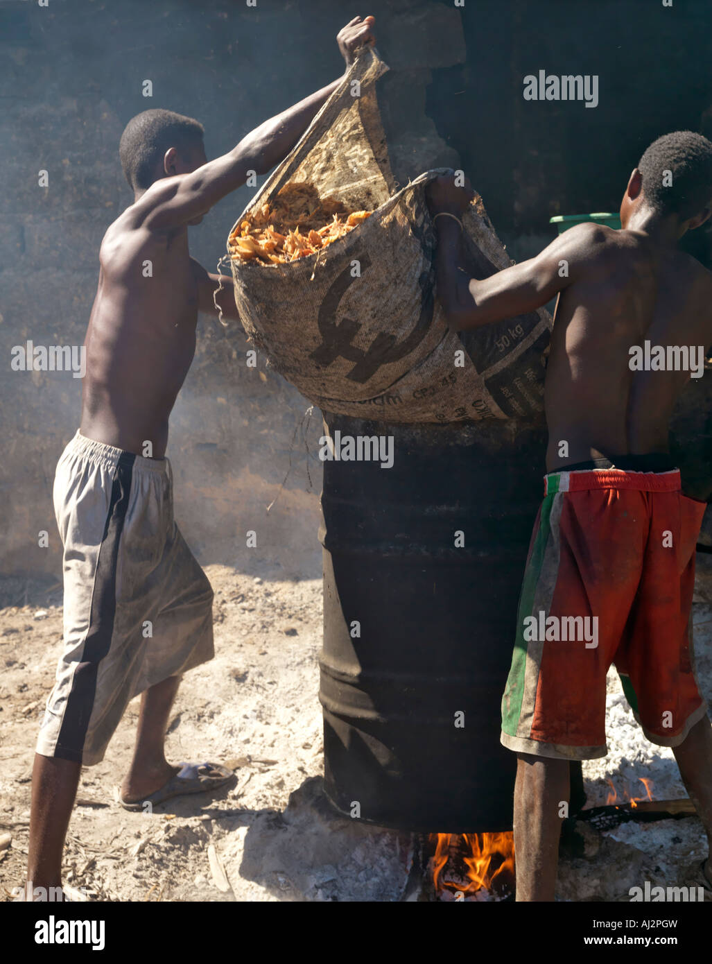 Men tip sugar cane pulp into a drum for boiling with water as the first ...