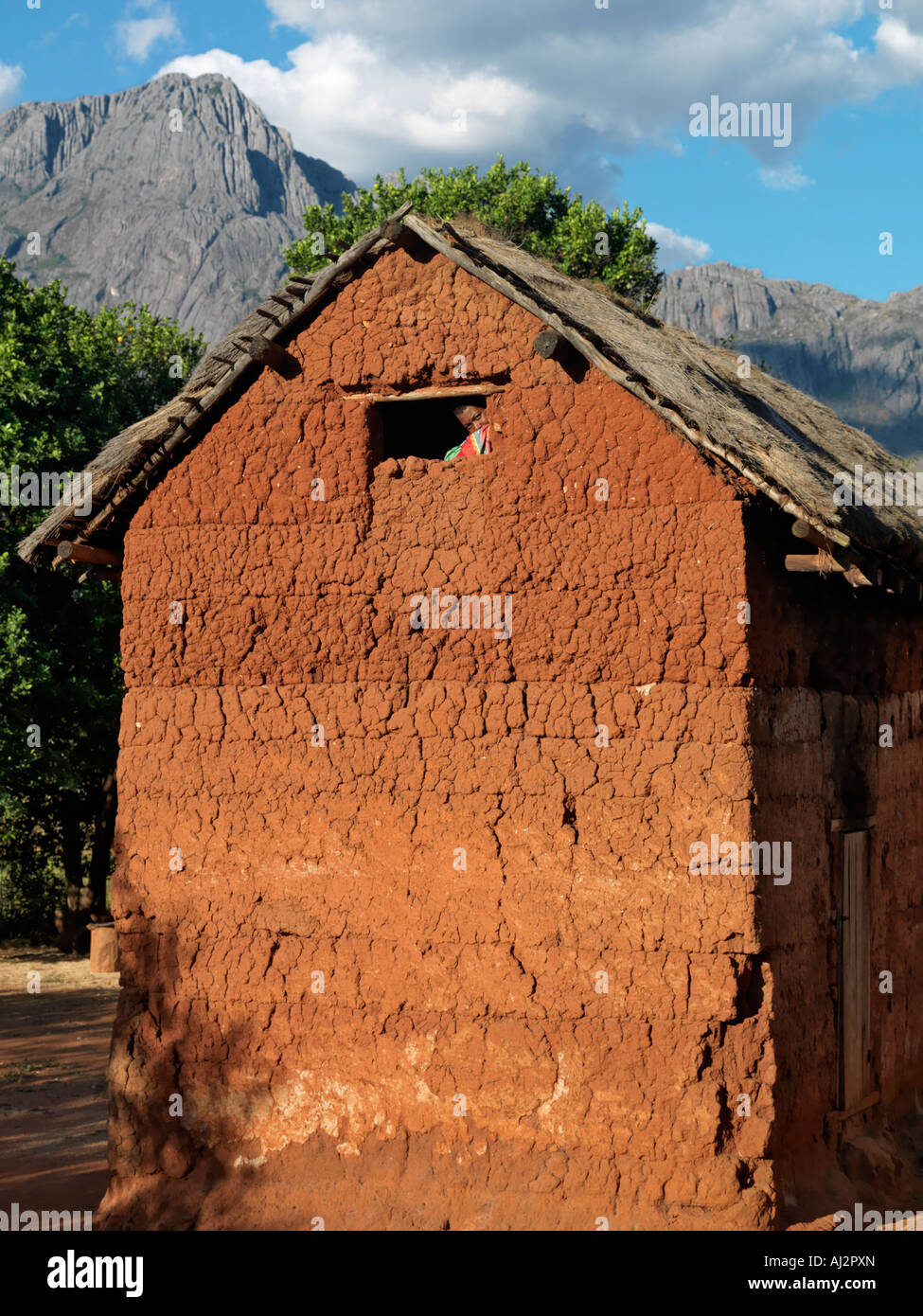 A man peeps out of the top window of a typical double-storied house of the Betsileo people in the Southern Highlands Stock Photo