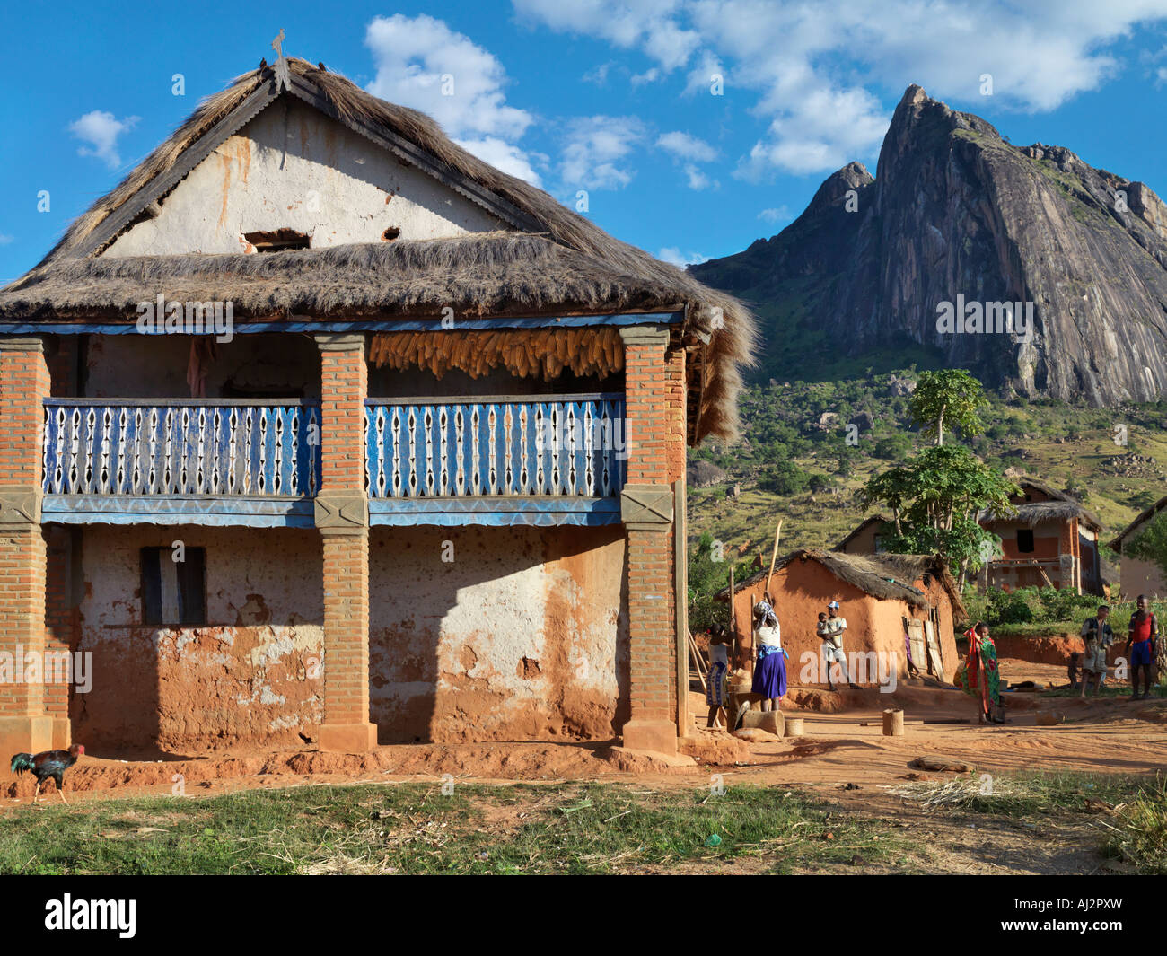 Women pound corn beside a typical double-storied house of the Betsileo people in the Southern Highlands of Madagascar. Stock Photo