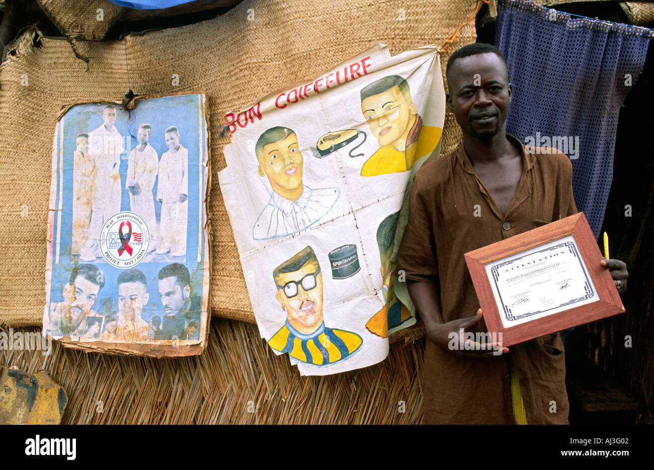 A Barber posing outside his makeshift shop, showing his hairdressing diploma. Mopti, Mali Stock Photo