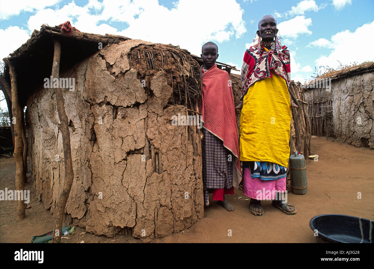 Maasai grandmother and granddaughter posing outside their small traditional house made of mud and cow manure. Kajiado, Kenya Stock Photo