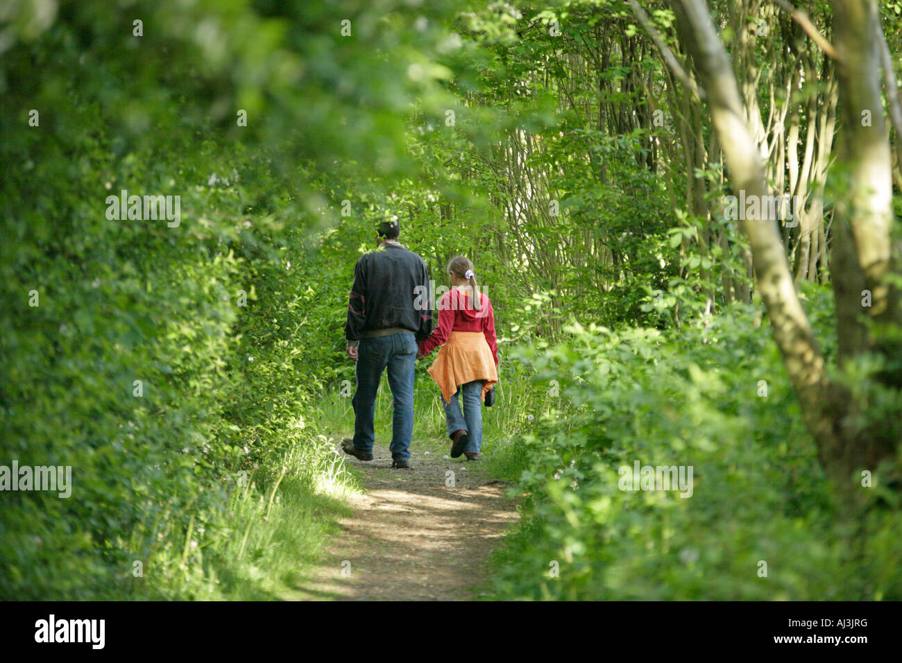 a man walking along a forest path holding a young girl by her hand Stock Photo