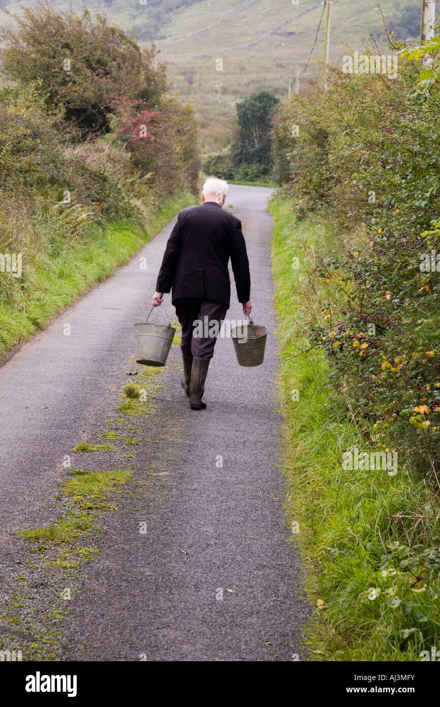 Stock photo of a farmer walking away from camera carrying a bucket in each hand Shot October