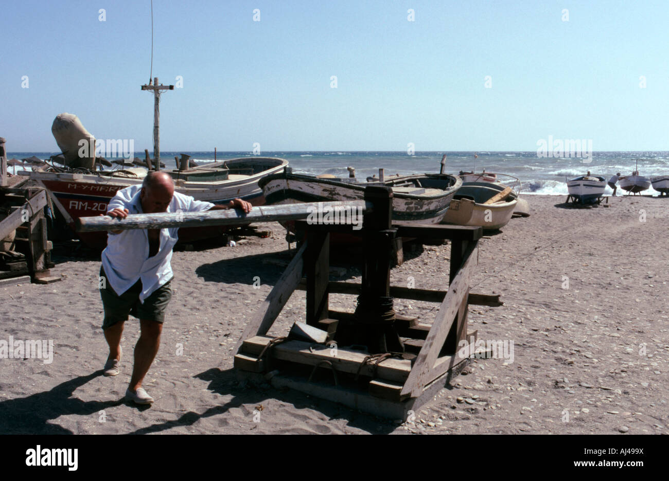 Man operating a winch to haul fishing boats onto the beach at Cabo de Gata Almeria Province in Southern Spain Stock Photo