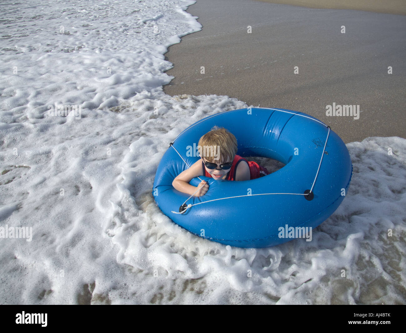 boy playing on beach with blue tube float floatation device waves