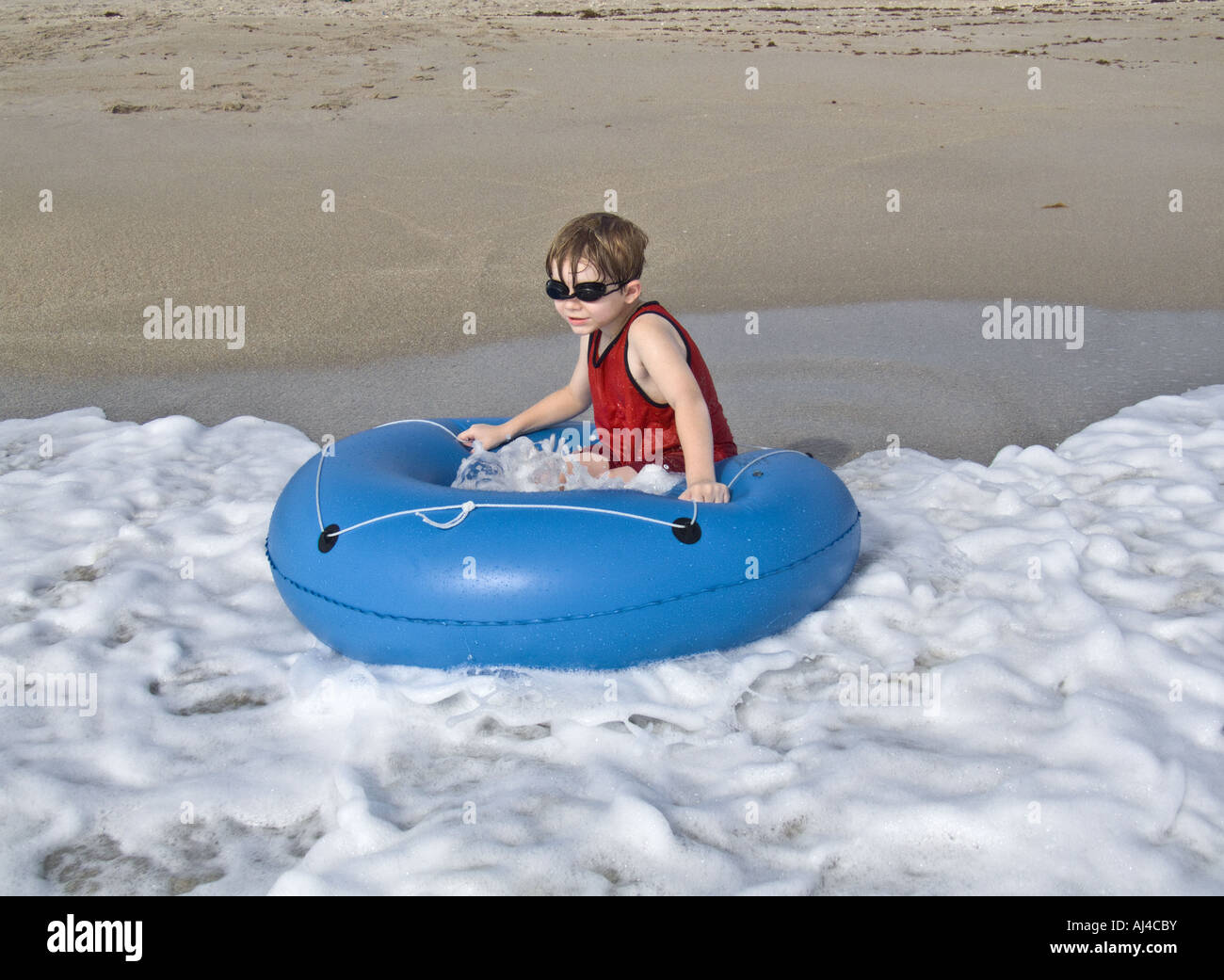 boy playing on beach with blue tube float floatation device waves