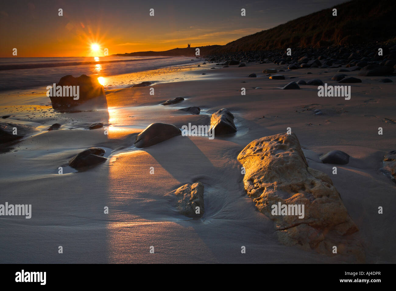 Golden early morning sunshine lights up the sandstone boulders on Dunstanburgh beach, Northumberland Stock Photo