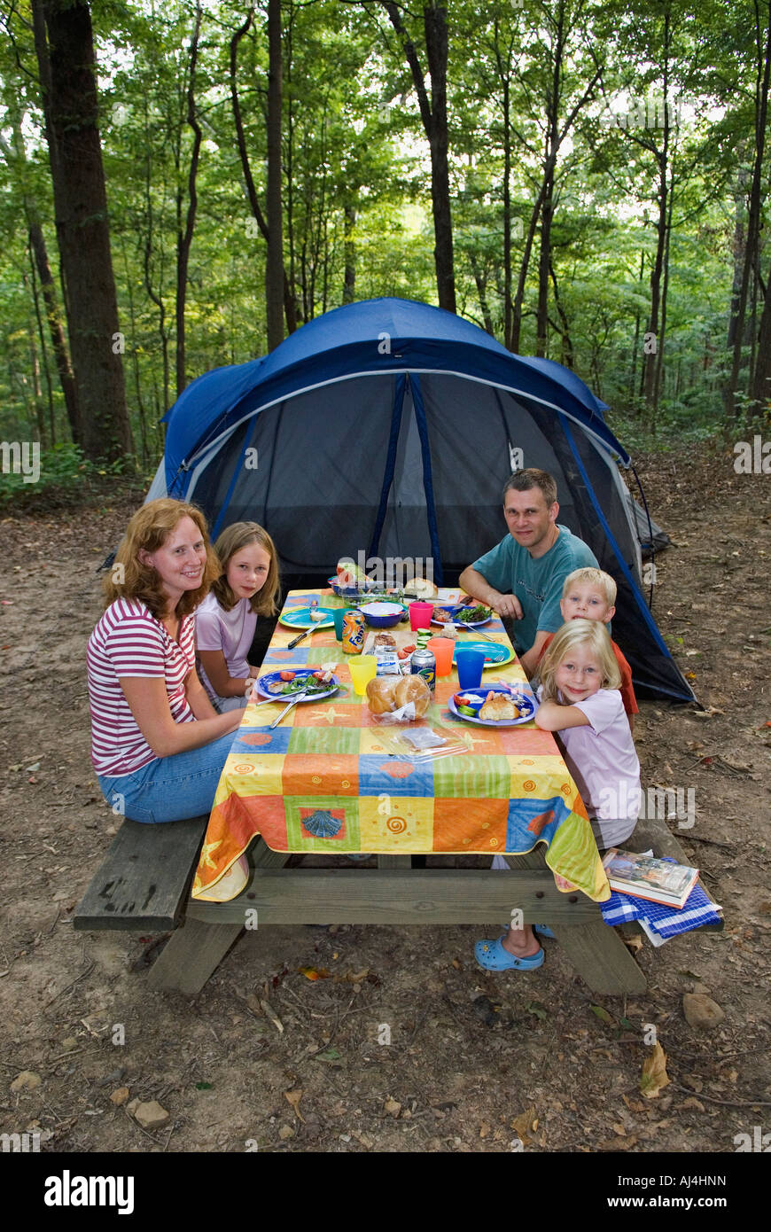 Camping Family Eating Dinner at Picnic Table with Tent in the