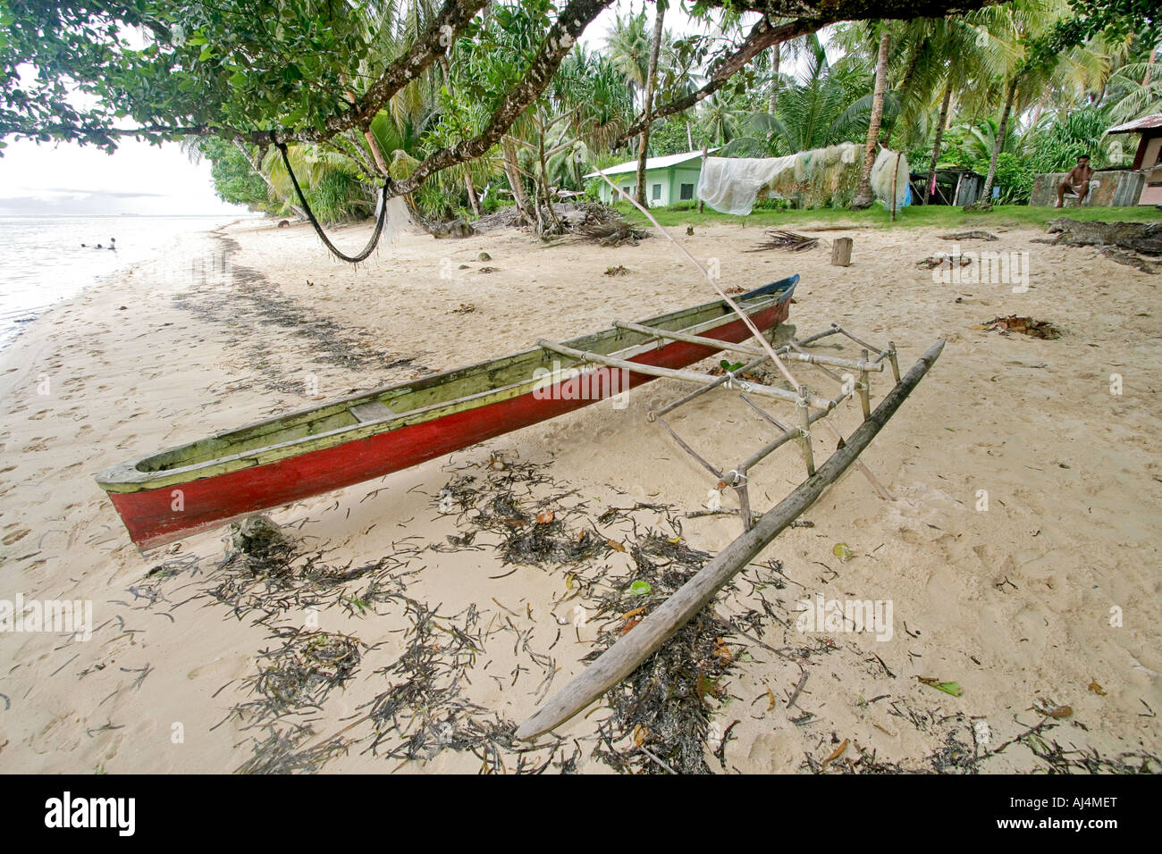 Traditional hand carved outrigger canoe sits on beach in front of house in isolated Kosrae village in Micronesia Stock Photo
