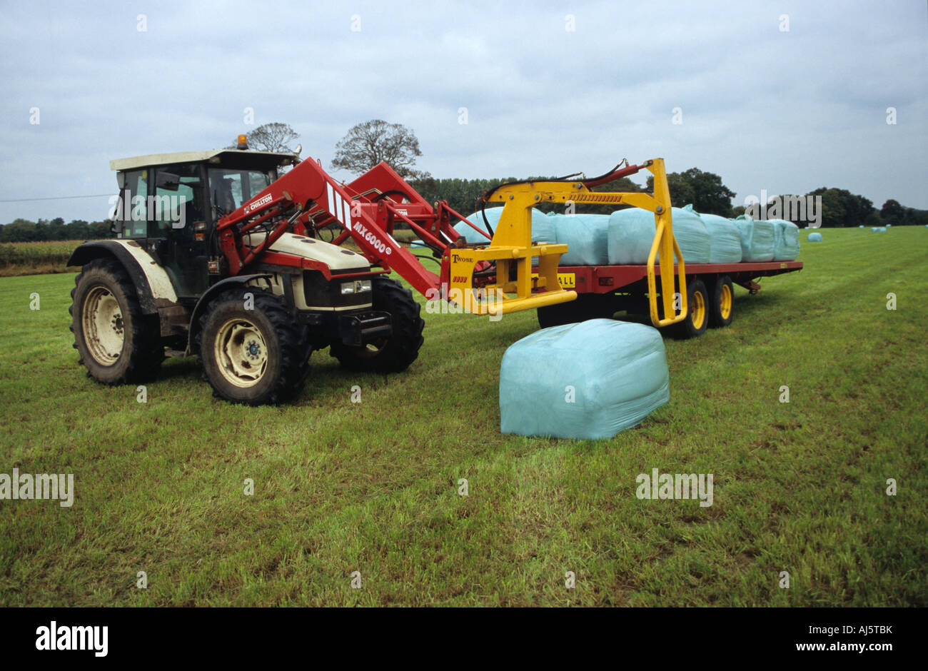 Farmer Placing Plastic Covered Hay Bales On The Back Of A Trailer Using A Tractor Stock Photo