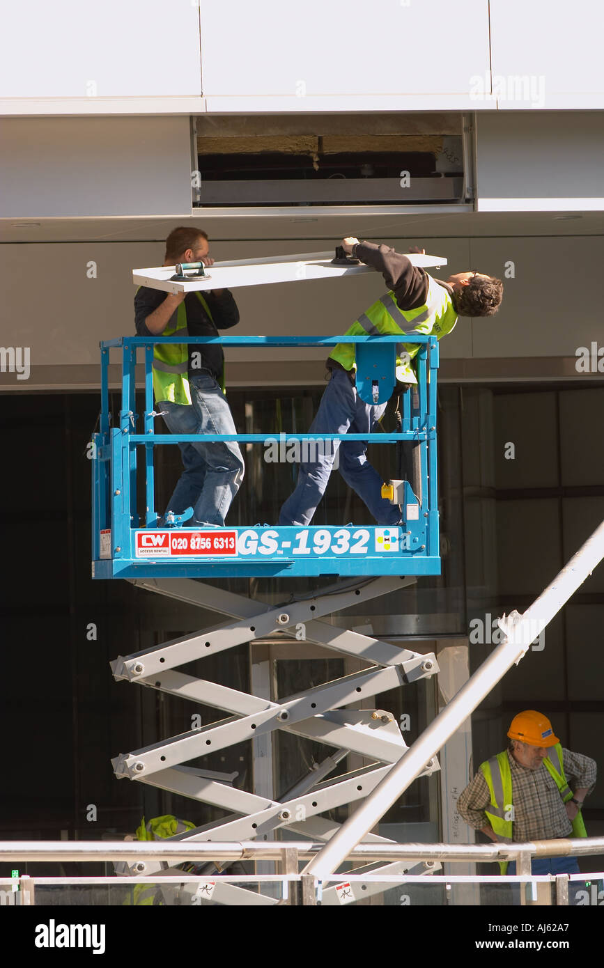 Workmen on scissor lift attaching metal cladding to new office building Stock Photo