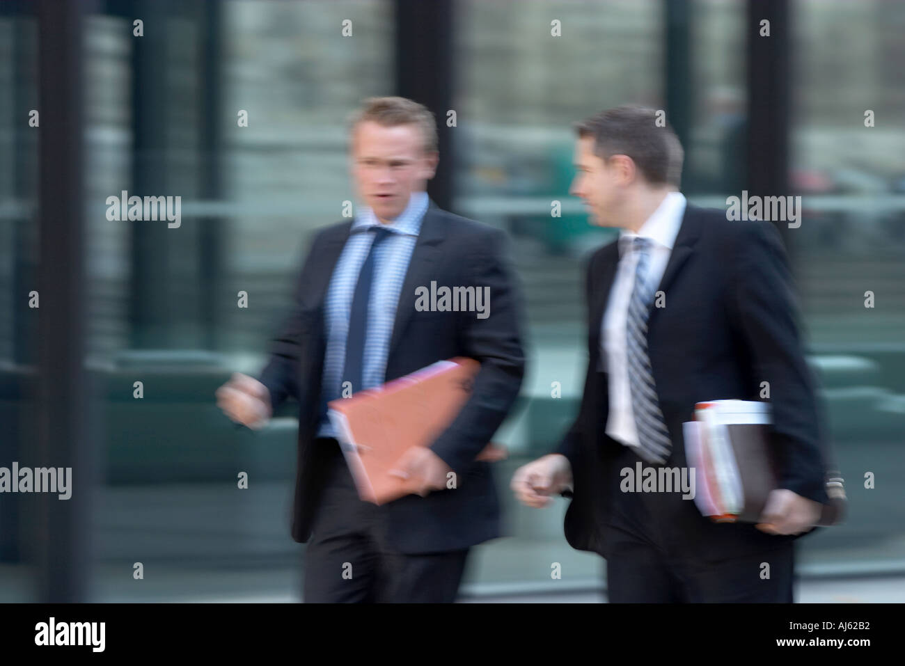 Two businessmen walking and talking carrying paperwork Stock Photo - Alamy