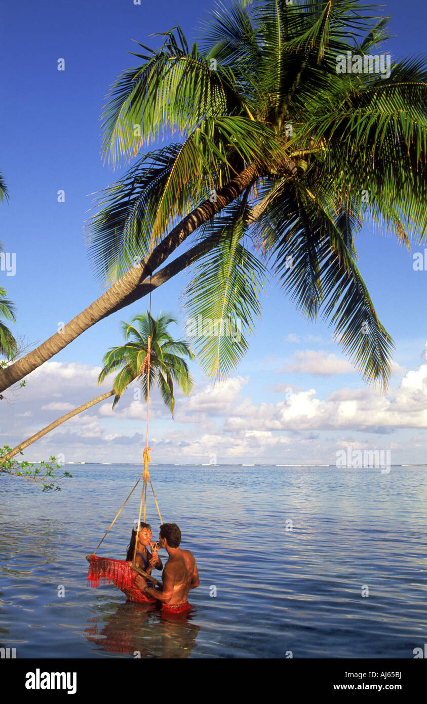 Couple sharing tropical drink in swing hanging from palm tree on Meeru Island in Maldives Stock