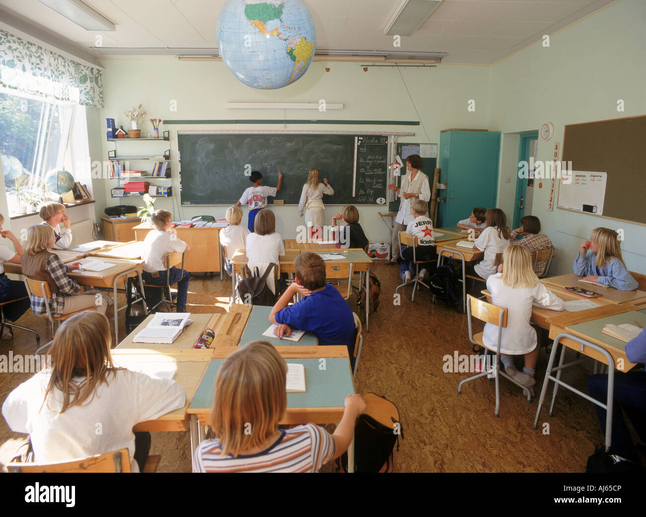 Elementary school children at desks and blackboard in Swedish classroom below world globe Stock Photo