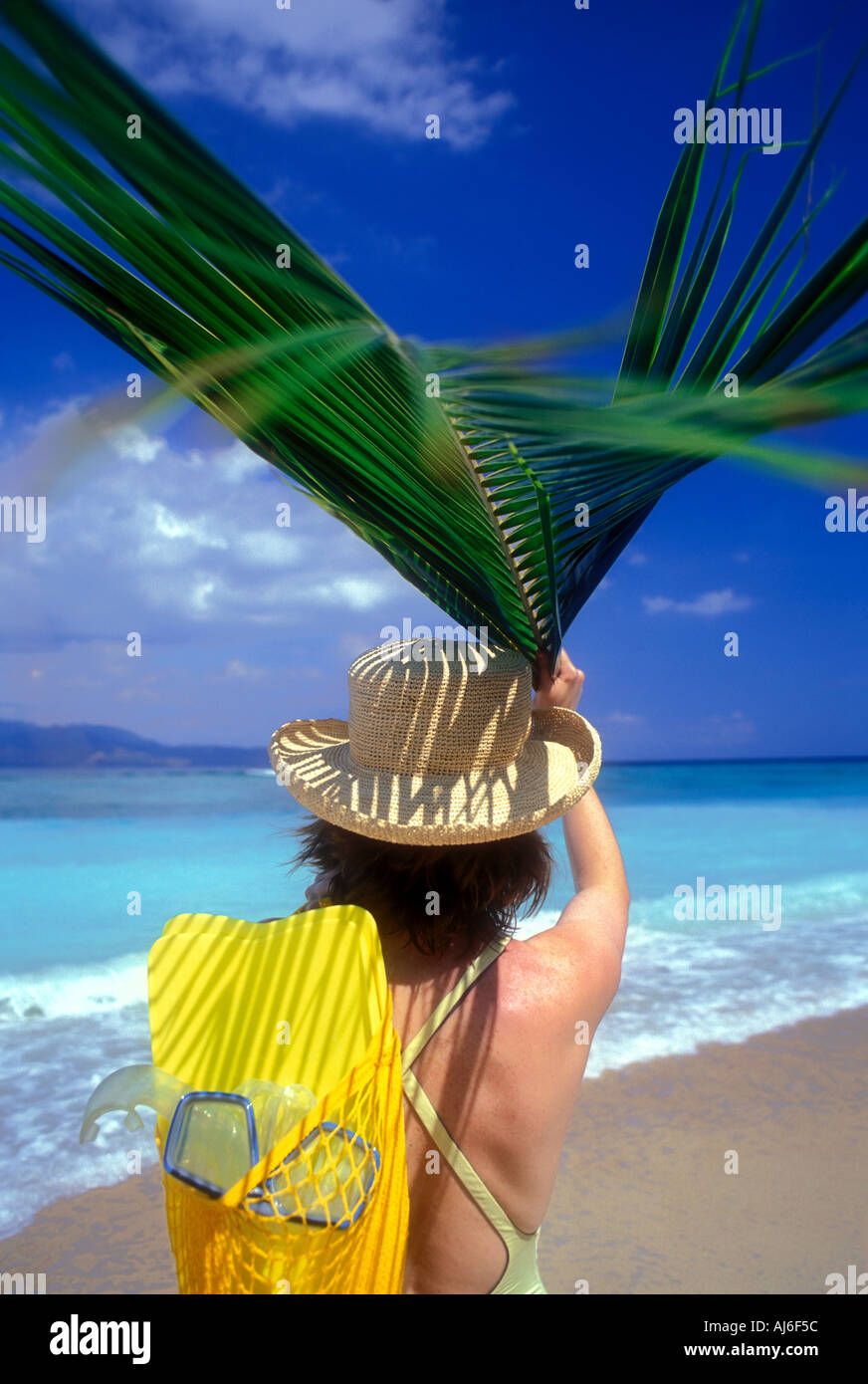 Woman on beach holding palm frond leaf over head on the island of Lombok in Indonesia Model Released Image Stock Photo