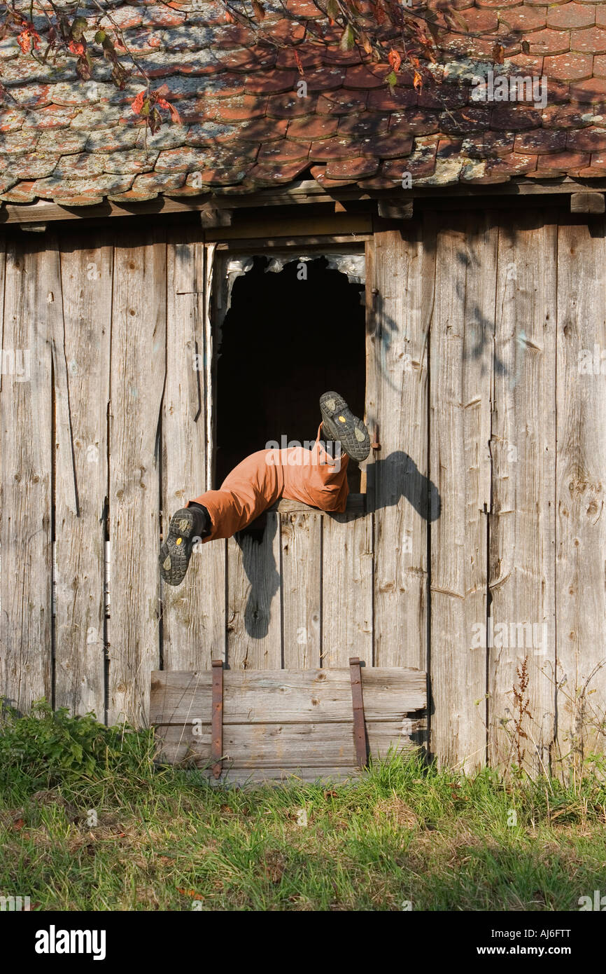 Woman climbing through a window of an abandoned wooden hut Weingarten