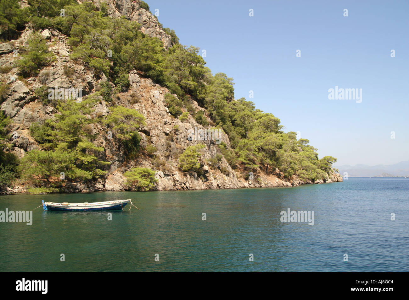 Small traditional fishing boat moored beneath a cliff near Fethiye Turkey  Stock Photo