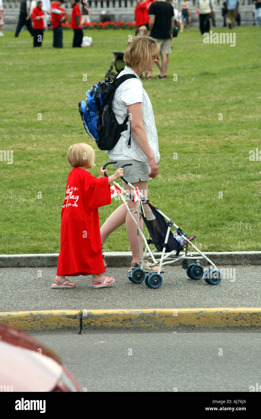 Little girl in a long red T shirt pushing a stroller in downtown Victoria  during Canada Day celebration Stock Photo - Alamy