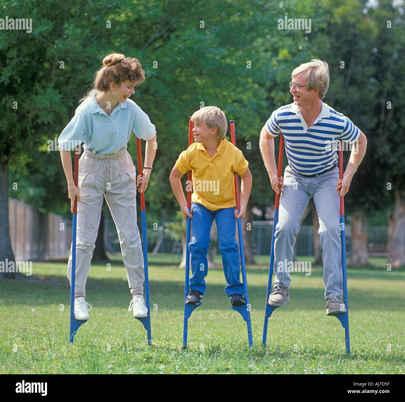 family of three walking on stilts in park Stock Photo