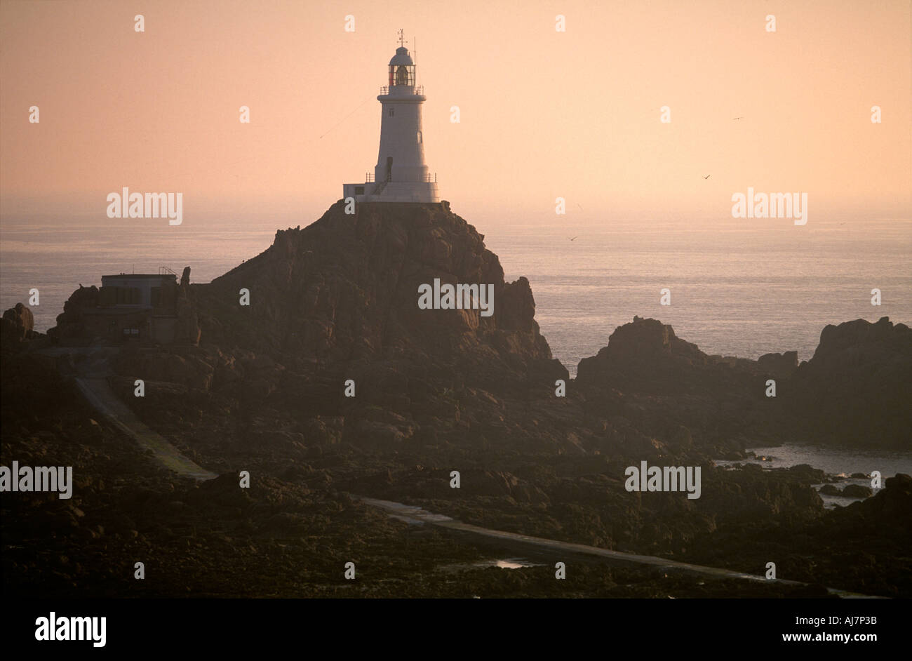 Corbiere lighthouse stands firm on rocks at low tide in late afternoon summer sunshine La Pulente Jersey UK First lighthouse to be built of concrete Stock Photo