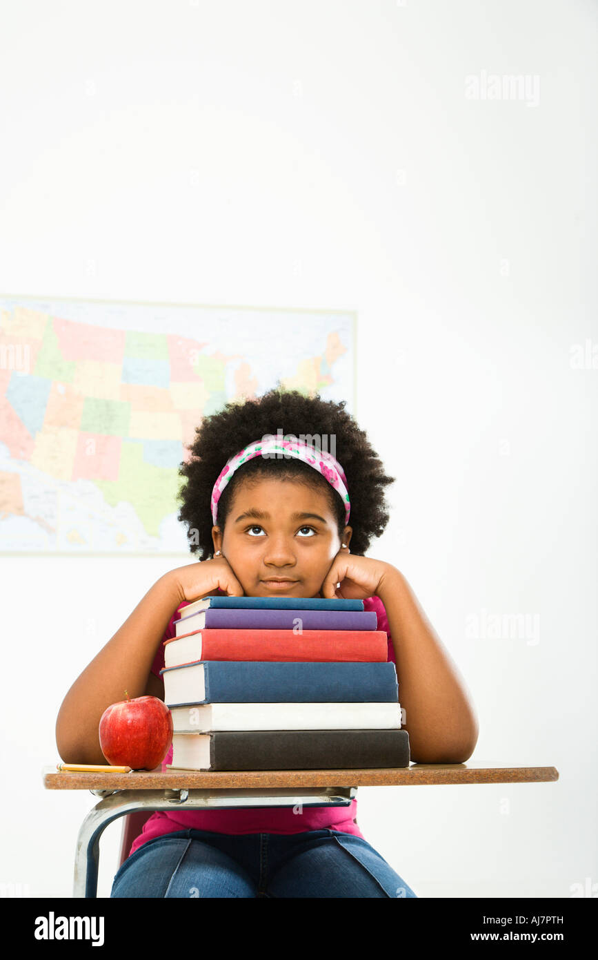 African American girl sitting in school desk with large stack of books