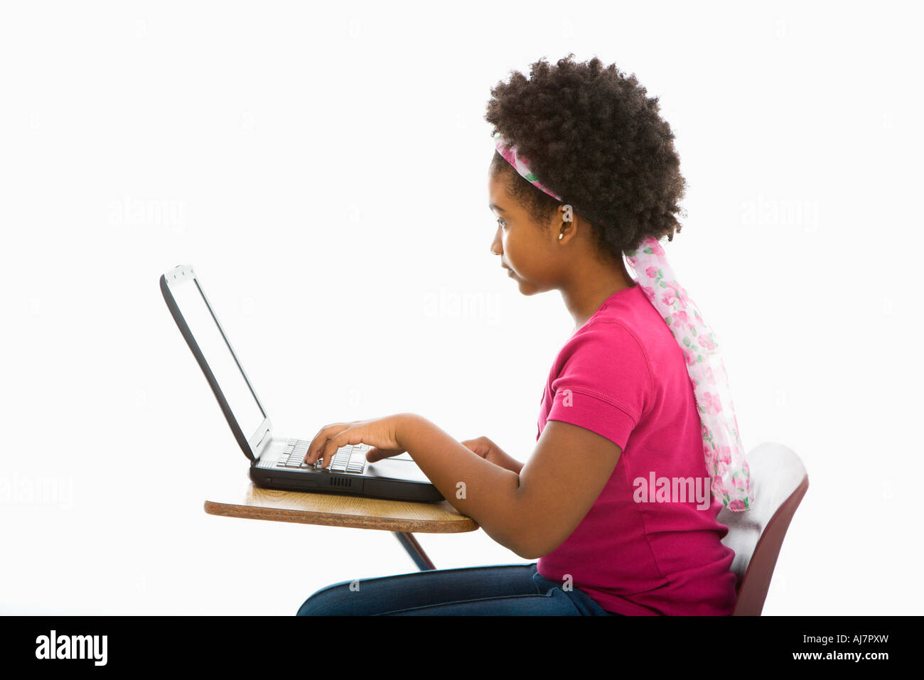 Side view of African American girl sitting in school desk typing on ...