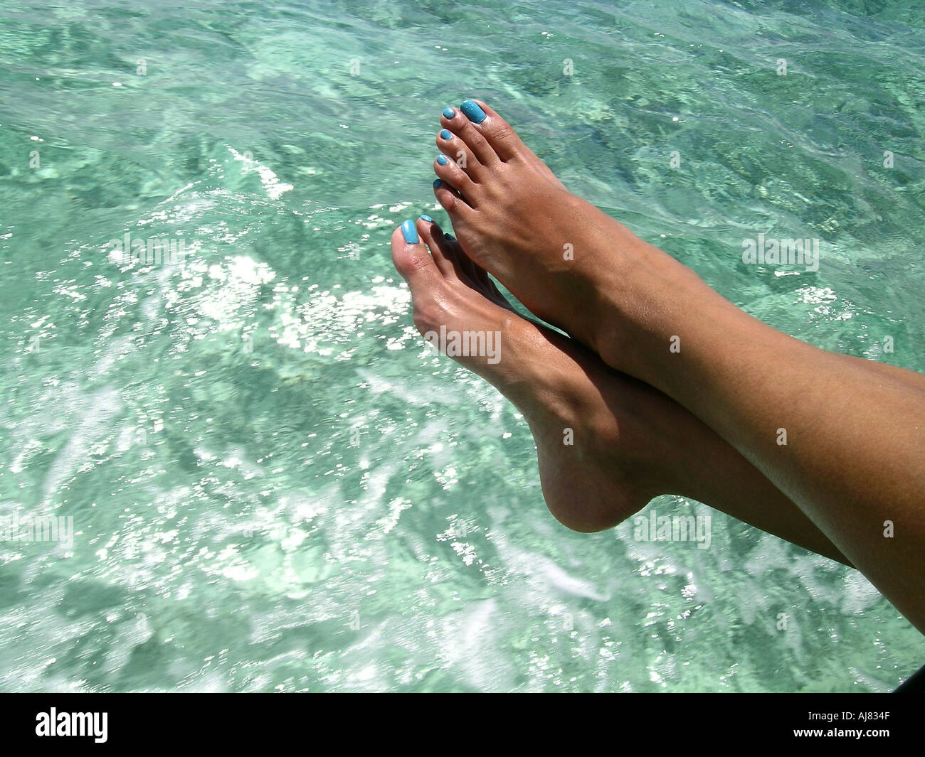 Woman's blue painted toenails & feet against clear sea water, Mauritius