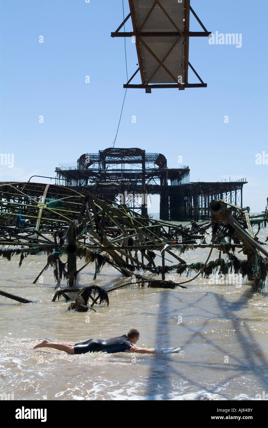 A surfer paddles through the remains of the West Pier, Brighton, Sussex, England. Stock Photo