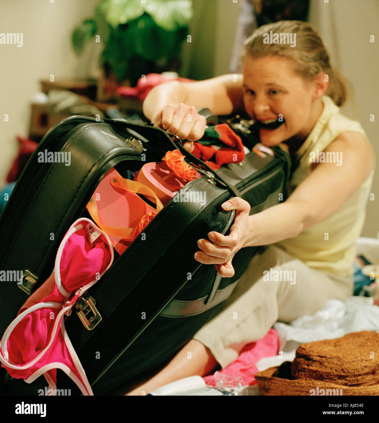 woman struggling to do up suitcase in bedroom Stock Photo