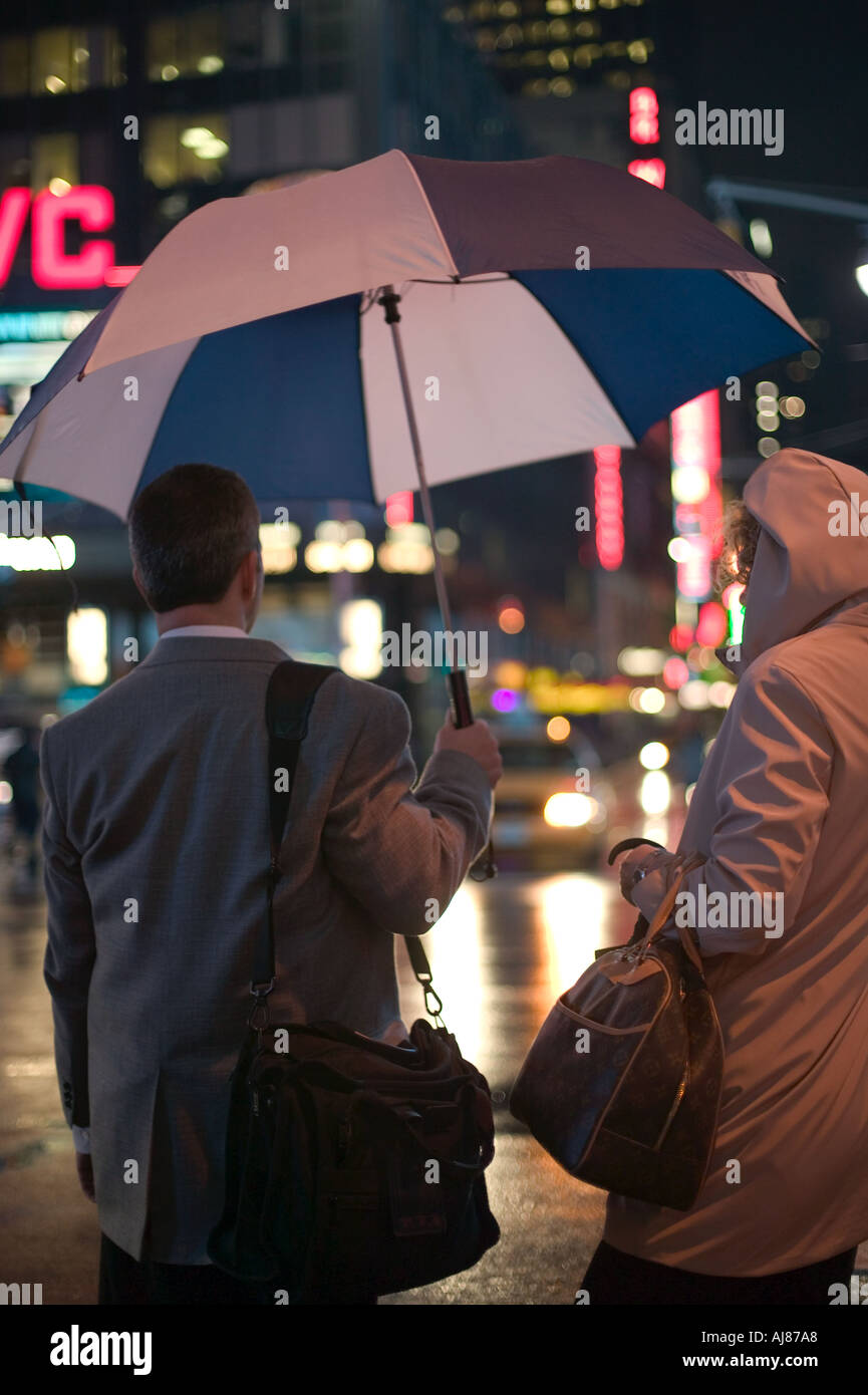 Couple crossing Broadway carrying umbrellas on rainy night in Times ...