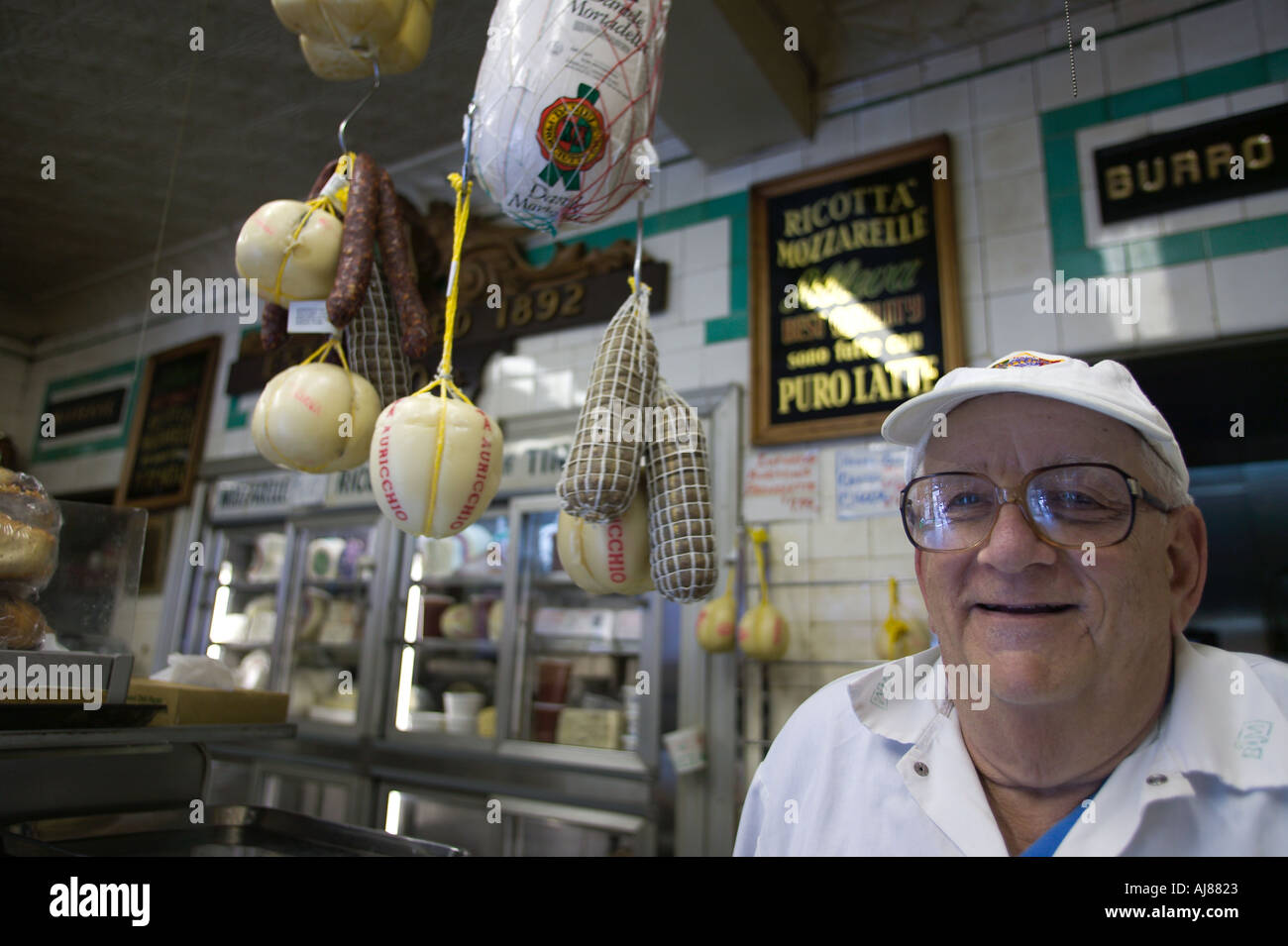 Cheeses and salamis hang next to the owner of the Alleva Dairy on corner of Grand and Mulberry Streets New York NY Stock Photo