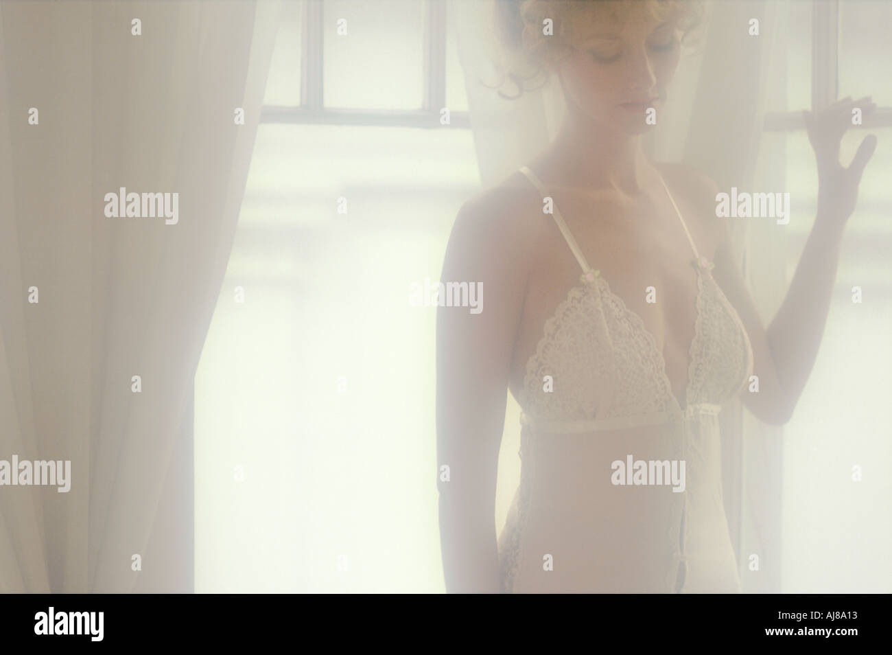 Woman by window in romantic white lingerie Stock Photo