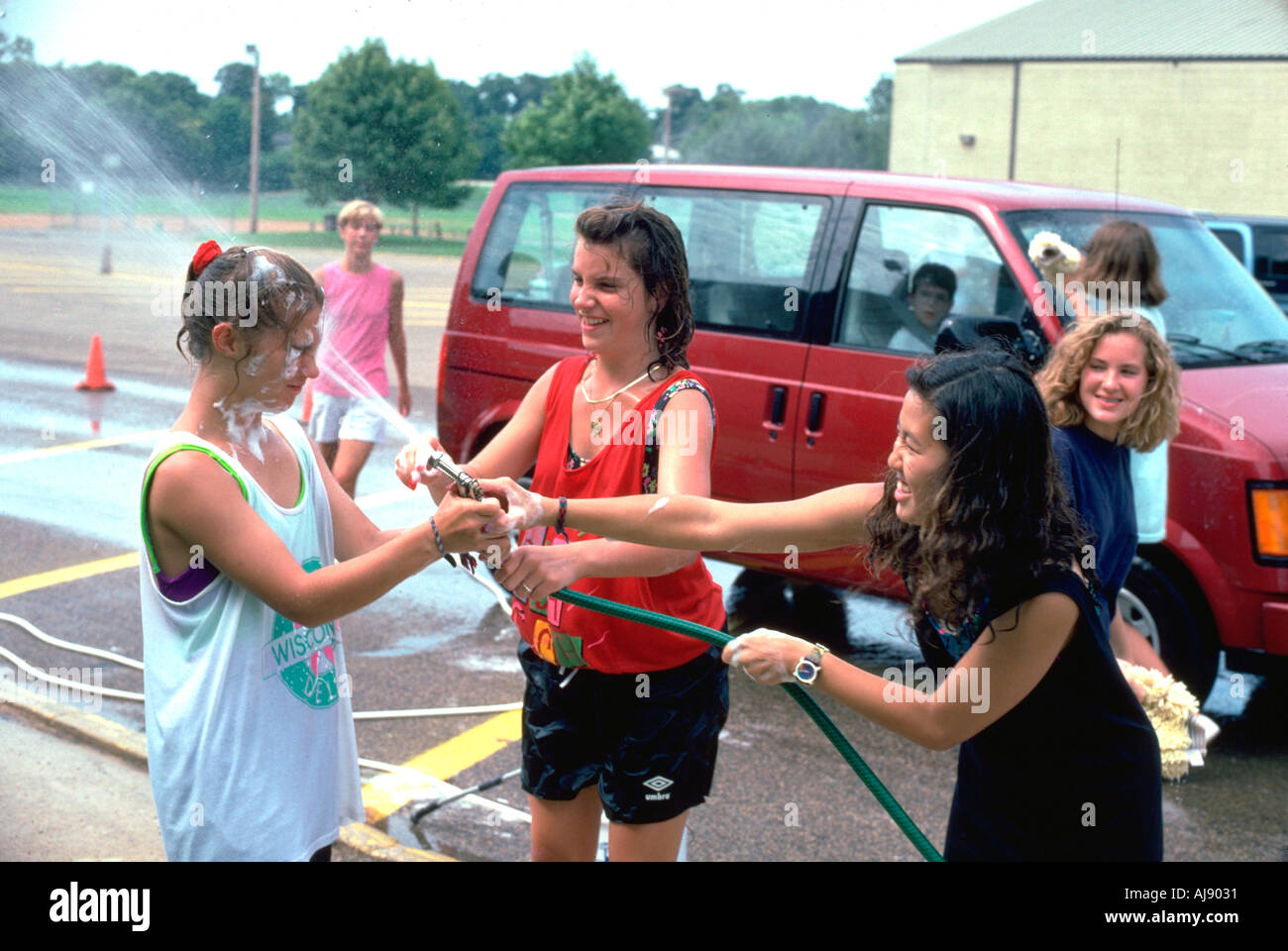 Asian teen spraying white friends age 15 at car wash fund raiser. Mound Minnesota USA Stock