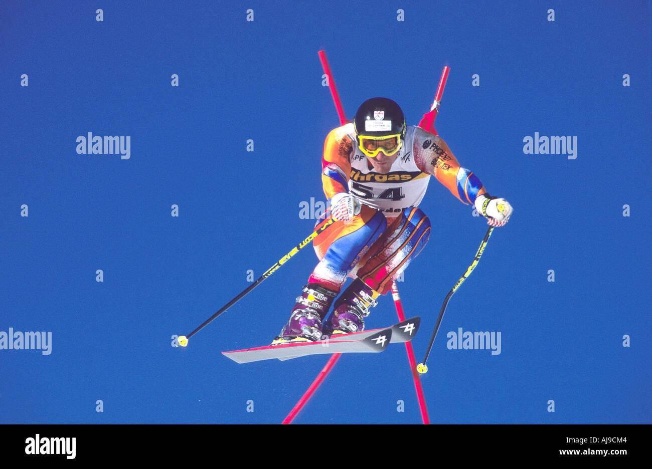 Ski racer in air over jump flashes past race flag Stock Photo