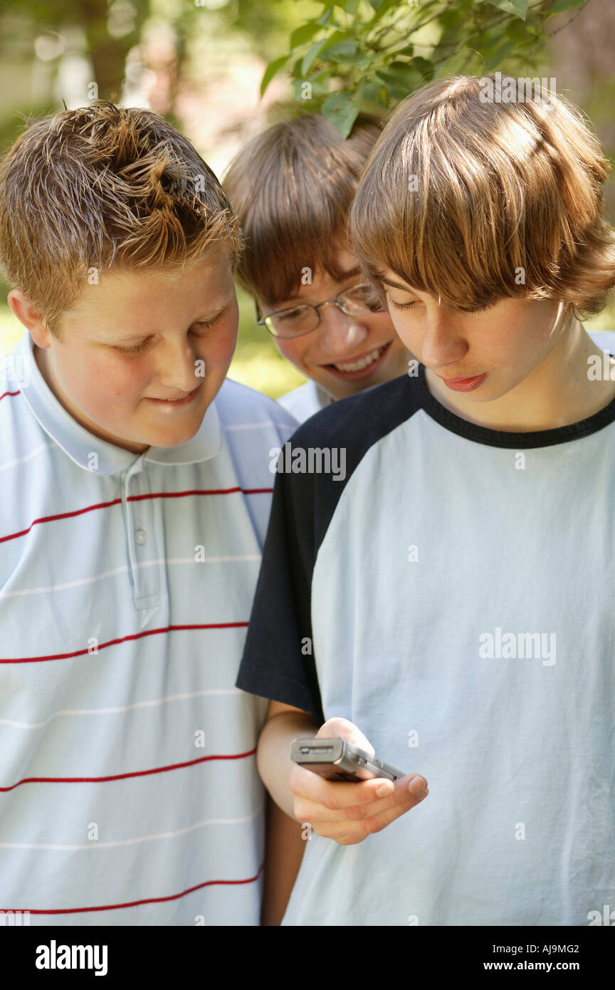 Three teenage boys huddled together using mobile phone Stock Photo