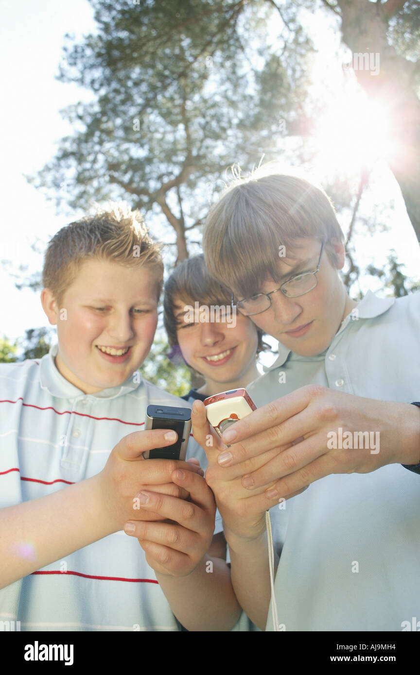 Three teenage boys huddled together using mobile phones Stock Photo